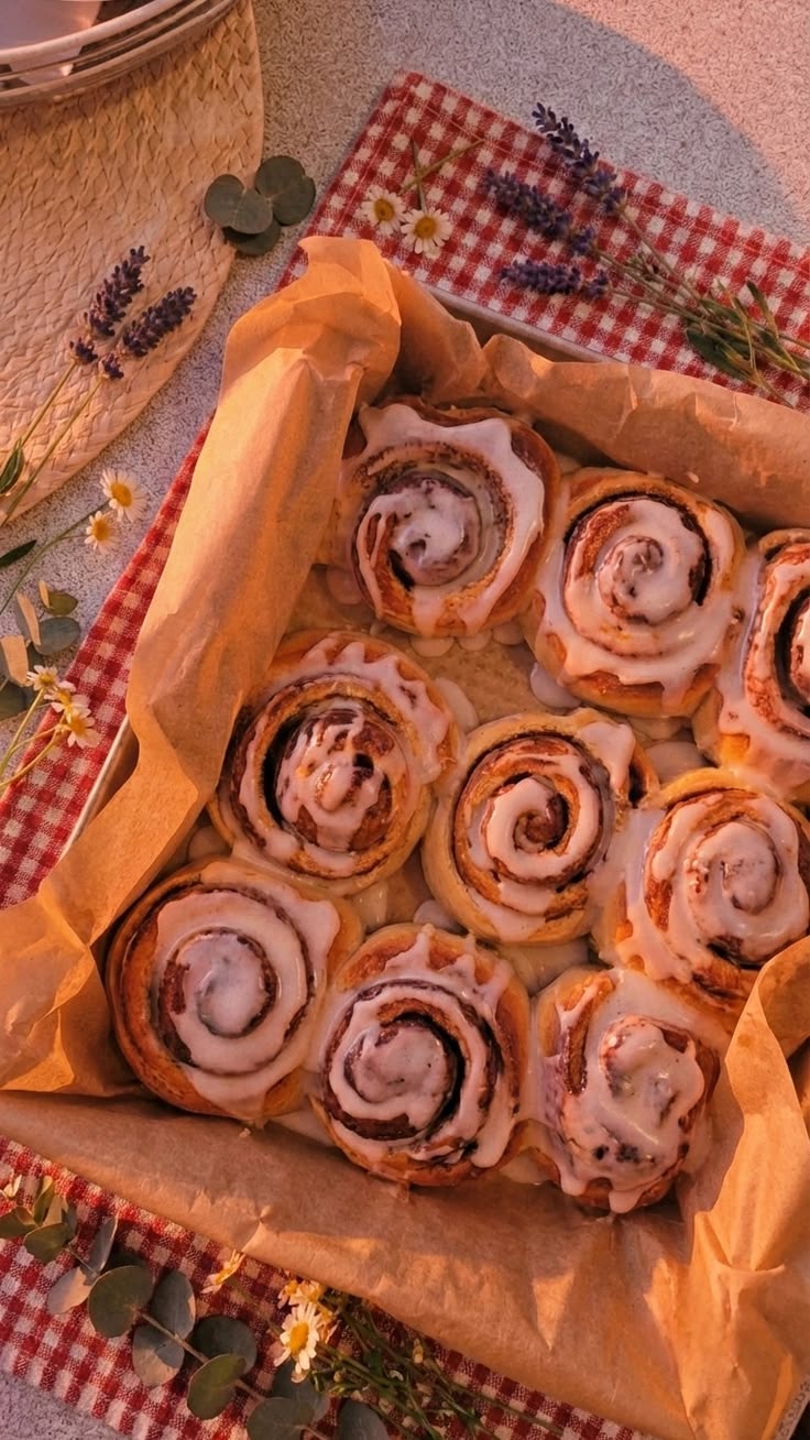 Pan of iced cinnamon rolls on parchment with gingham cloth and wildflowers